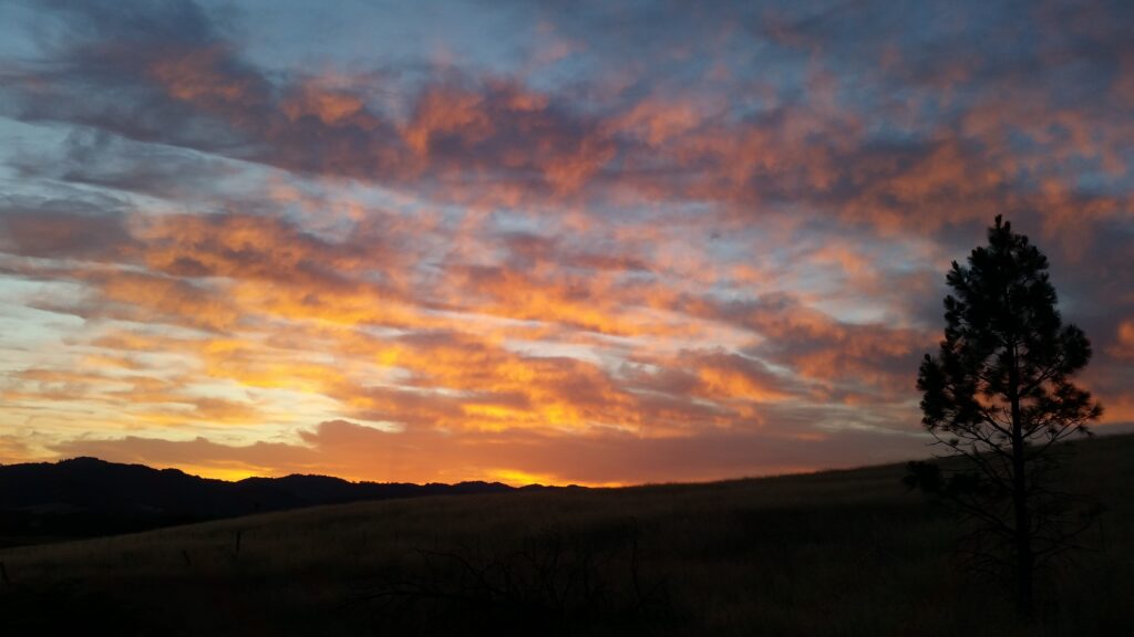 A sunset of flaming clouds hangs over a landscape in silhouette. 