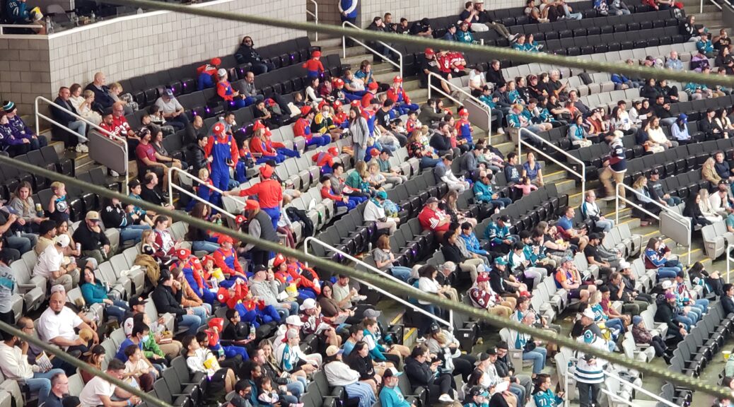 A crowd of people gathered to watch a hockey game. For some reason there are many people dressed like Mario from Donkey Kong.
